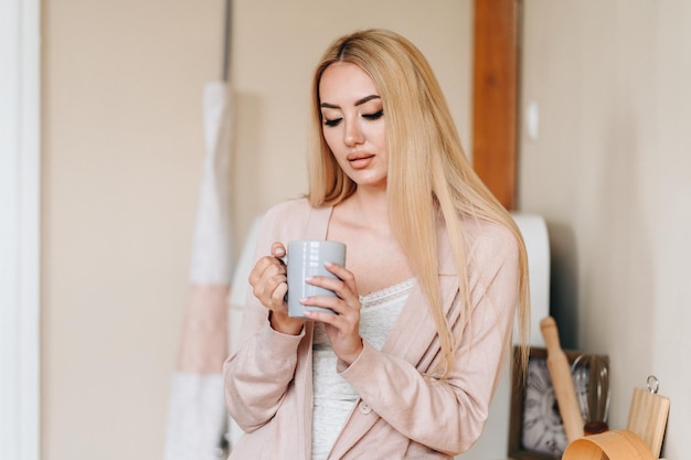 La mujer joven comienza su mañana con una taza de café La mujer sostiene una taza de luz natural desde la ventana