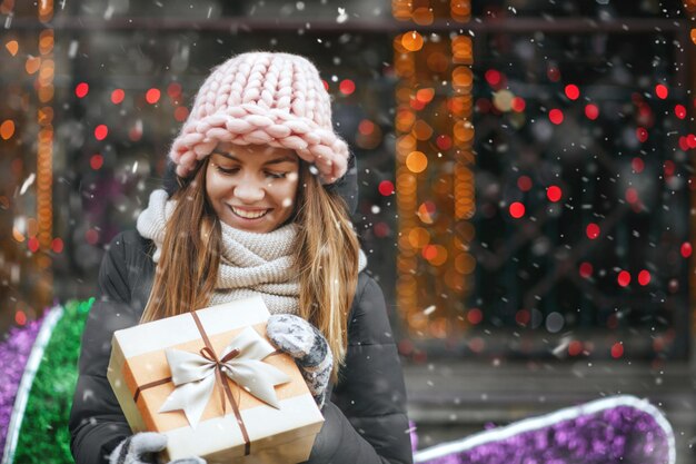 Mujer joven complacida recibiendo un regalo en la calle contra el escaparate decorado