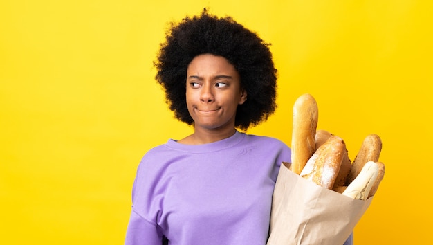 Mujer joven comprando algo pan aislado en amarillo teniendo dudas mientras mira hacia arriba