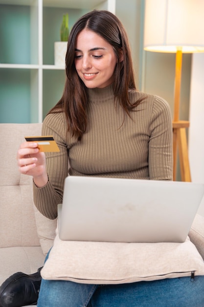 Mujer joven comprando en línea con una tarjeta de crédito y usando una computadora portátil vertical