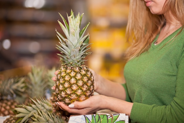 Mujer joven comprando piña en un supermercado.