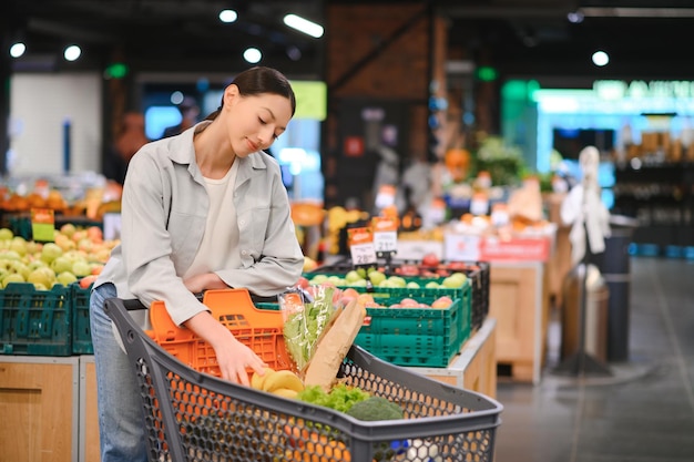 Mujer joven comprando verduras en el mercado de comestibles