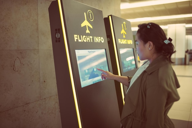 Mujer joven comprobando la hora en el quiosco de información de vuelos en el aeropuerto