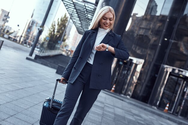 Mujer joven comprobando su reloj y tirando de la maleta