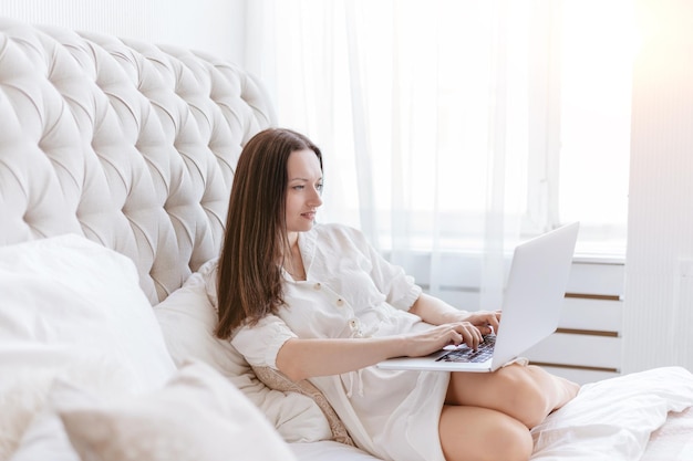 mujer joven, con, computador portatil, sentado, en la cama, en, ella, dormitorio