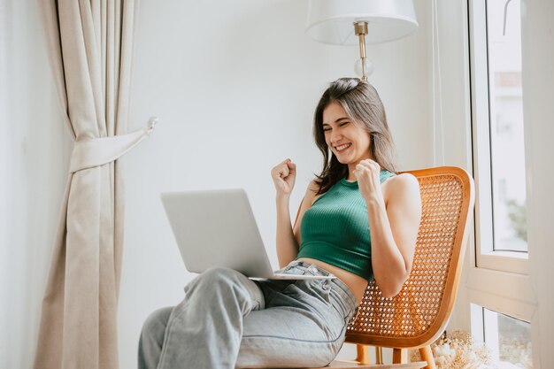 Foto mujer joven con computadora portátil en casa feliz alegre éxito ganar expresión positiva