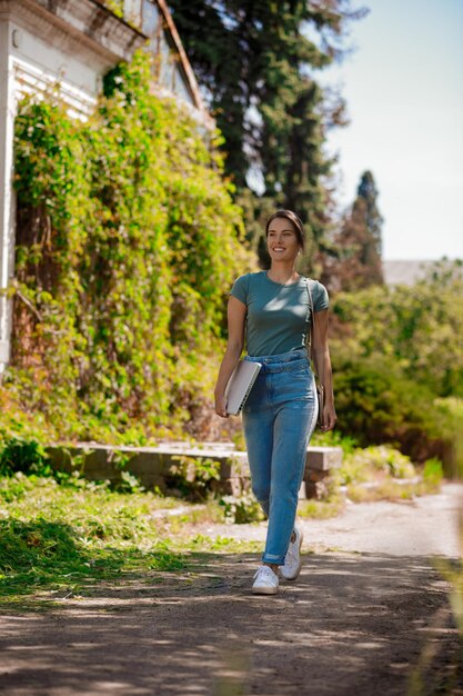 Mujer joven con una computadora portátil en las manos caminando en el parque