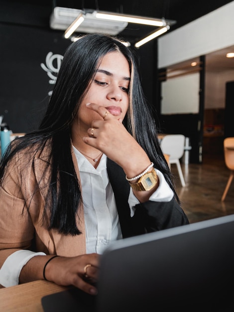 Mujer joven con una computadora portátil pensando y trabajando dentro de una moderna cafetería