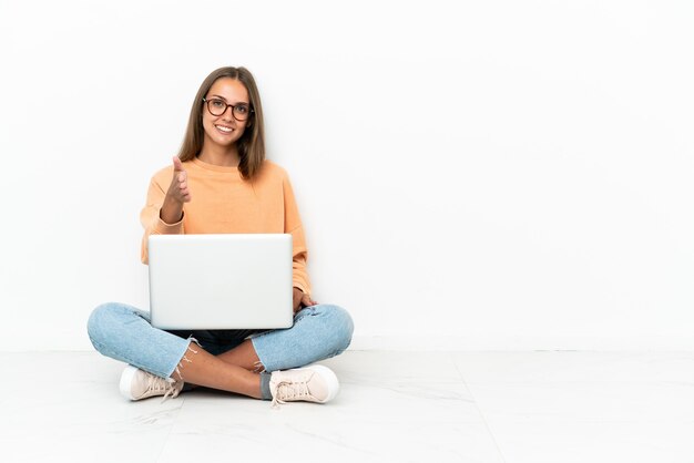 Mujer joven con una computadora portátil sentada en el suelo un apretón de manos para cerrar un buen trato