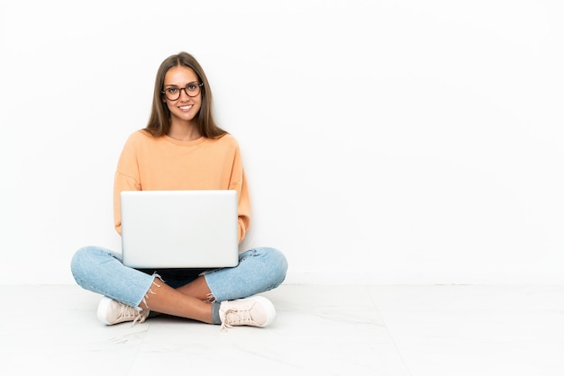 Mujer joven con una computadora portátil sentada en el suelo con los brazos cruzados y mirando hacia adelante