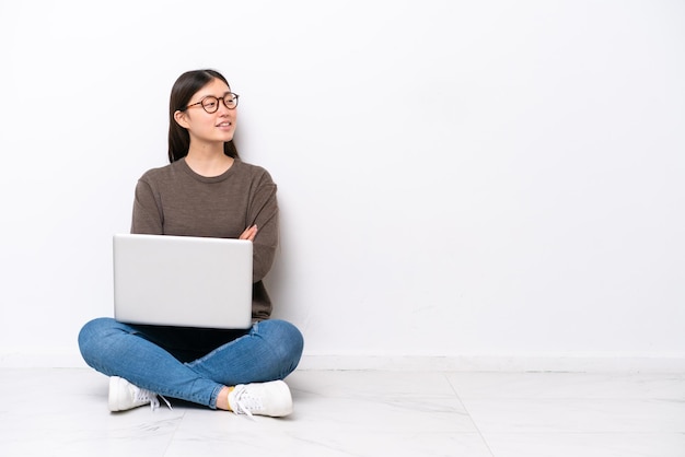 Mujer joven con una computadora portátil sentada en el suelo feliz y sonriente