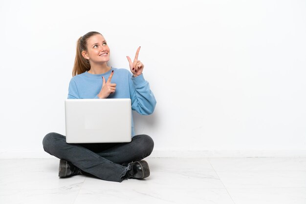 Mujer joven con una computadora portátil sentada en el suelo señalando con el dedo índice una gran idea