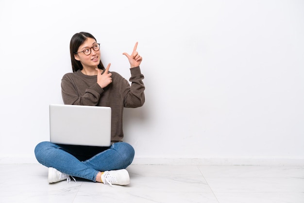 Mujer joven con una computadora portátil sentada en el suelo señalando con el dedo índice una gran idea