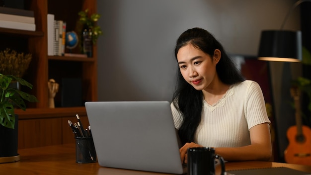 Mujer joven concentrada viendo una conferencia en línea durante el estudio en línea en una computadora portátil