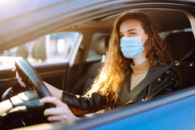 Mujer joven conduciendo un automóvil con una máscara médica durante una epidemia Aislamiento de transporte Covid2019