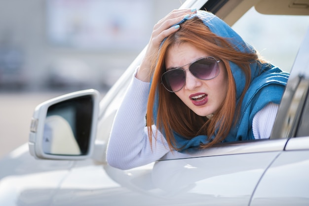 Mujer joven conduciendo un coche hacia atrás. Chica con expresión divertida en su rostro mientras hacía un daño en el guardabarros de un vehículo trasero.