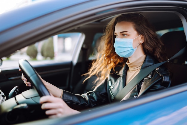 Mujer joven conduciendo un coche con una máscara médica durante una epidemia. Aislamiento de transporte. Covid-2019.