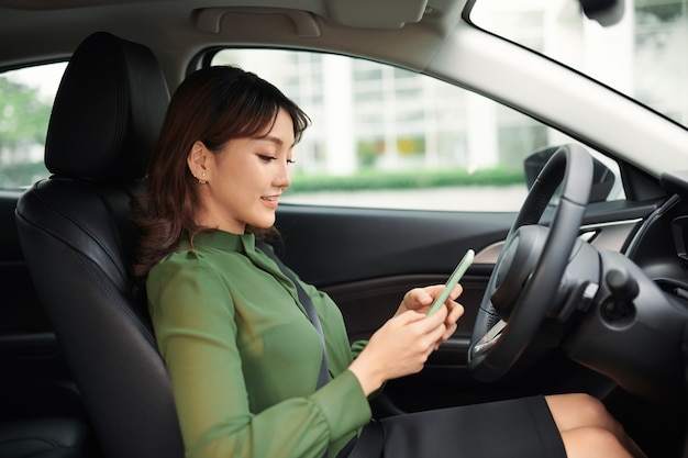 Mujer joven conduciendo un coche mirando la pantalla del teléfono