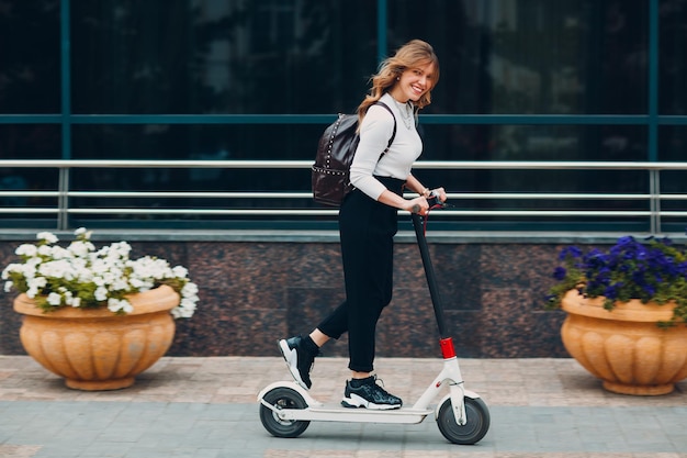 Mujer joven conduciendo scooter eléctrico en la ciudad