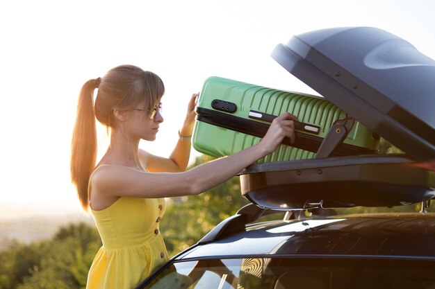 Foto mujer joven conductora poniendo maleta verde dentro del portaequipajes del coche concepto de viajes y vacaciones