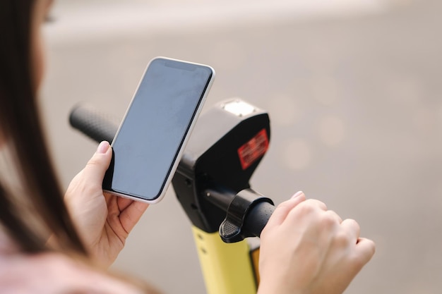 Mujer joven conectar un scooter eléctrico al aire libre mujer con teléfono para pago sin contacto