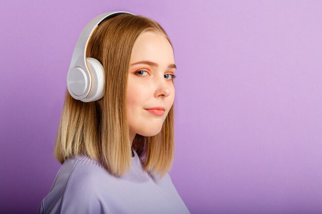 Mujer joven confiada en retrato de los auriculares. Hermosa mujer seria con peinado rubio disfruta de escuchar la música de la canción en los auriculares aislados sobre la pared de color púrpura. Copie el espacio.