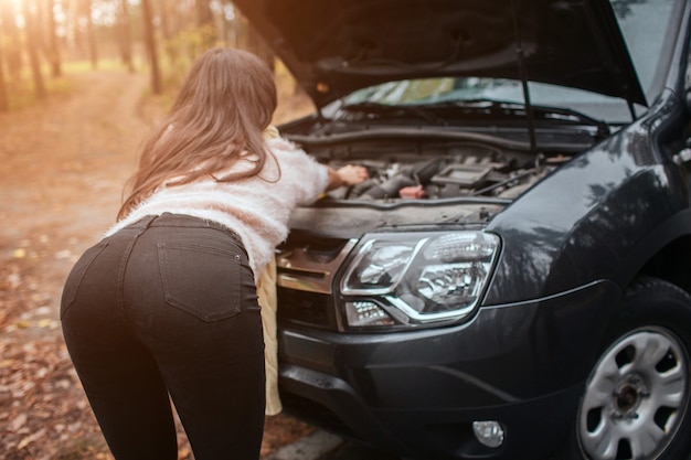 Mujer joven confundida mirando averiado reparación de automóviles de motor de coche en la calle.