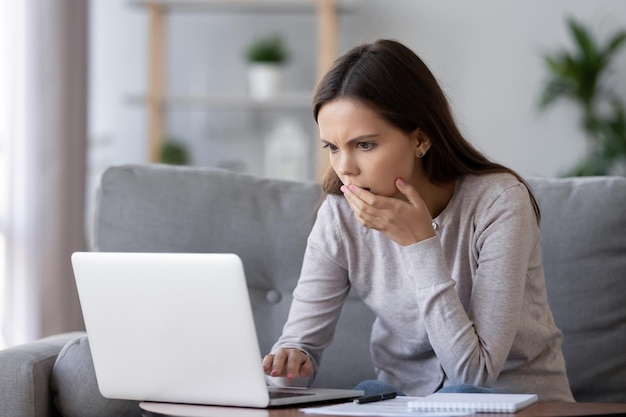 Mujer joven conmocionada y estresada leyendo malas noticias en línea mirando la pantalla rota de la computadora portátil confundida adolescente en pánico frustrada por un problema de computadora atascado error virus mensaje negativo en las redes sociales