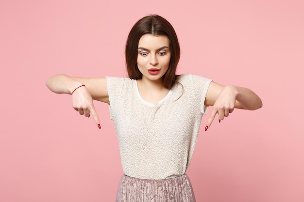 Foto mujer joven conmocionada con ropa ligera informal posando aislada en el fondo de la pared rosa, retrato de estudio. gente emociones sinceras concepto de estilo de vida. simulacros de espacio de copia. señalando con el dedo índice hacia abajo.