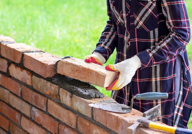 Mujer joven construye un muro de ladrillos, coloca ladrillos sobre mortero de cemento y arena