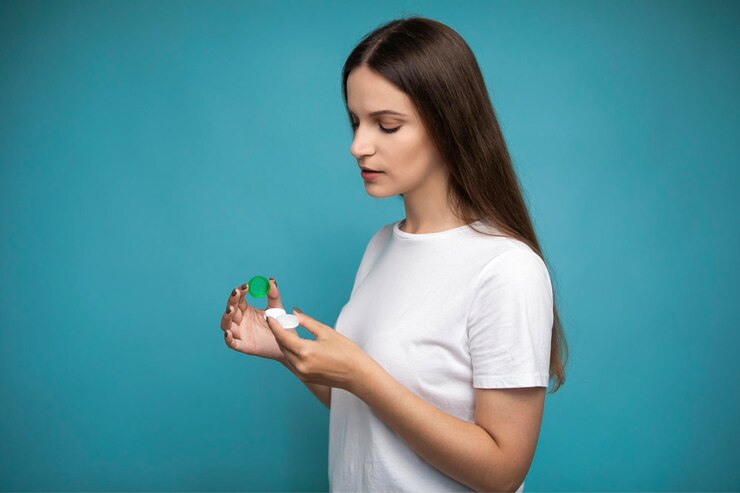 Mujer joven con contenedor de lentes de contacto sobre fondo azul.