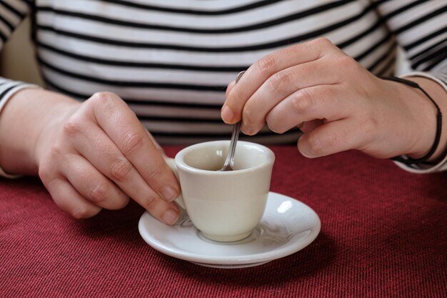 Una mujer joven convierte la cuchara en una taza de espresso. Detalle de las manos y la copa