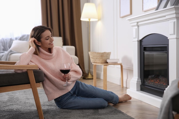 Mujer joven con una copa de vino descansando junto a la chimenea en casa