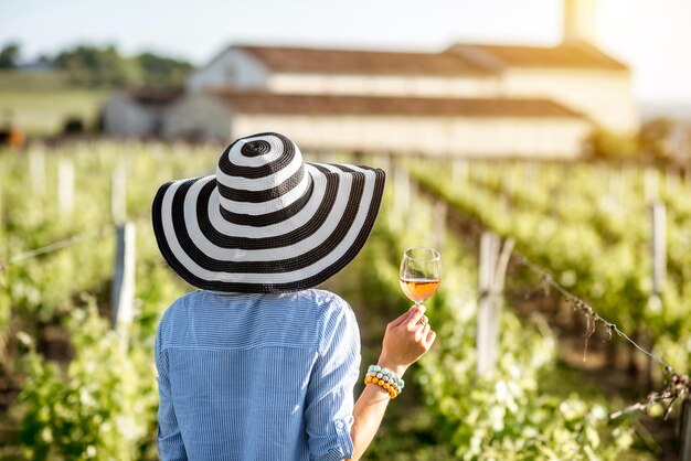 Mujer joven con copa de vino de pie en el hermoso viñedo durante la puesta de sol