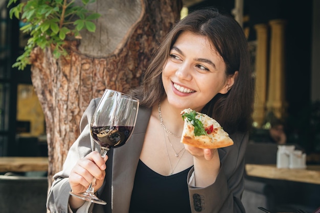 Una mujer joven con una copa de vino y un trozo de pizza en un restaurante.