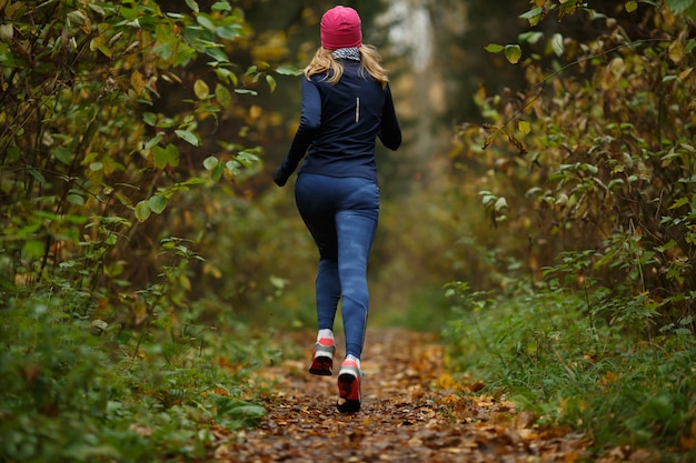 Mujer joven corre entre árboles en el parque otoño