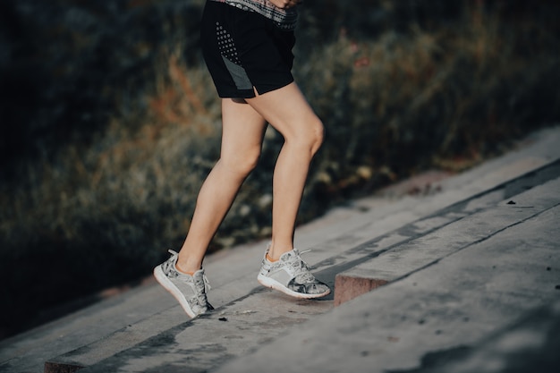 Mujer joven corre en el verano en la ciudad en el fondo de la escalera de carrera por la mañana