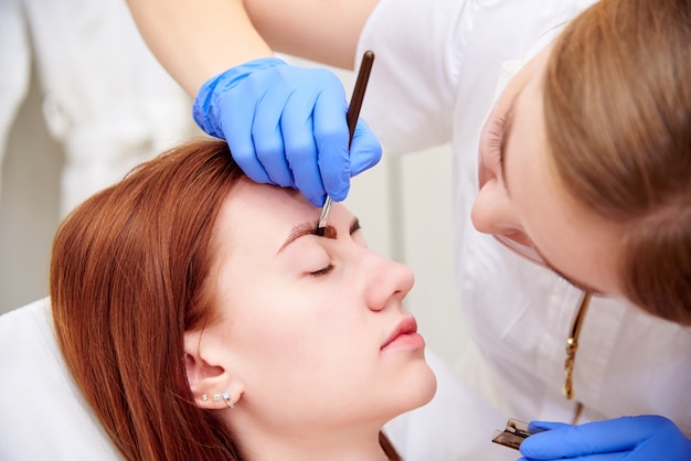 Mujer joven en corrección de cejas en clínica de cosmetología.