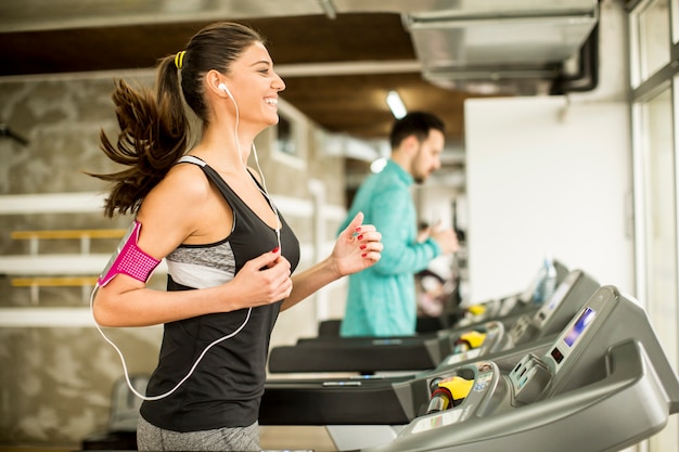 Mujer joven corriendo en la cinta y escuchando música en el gimnasio