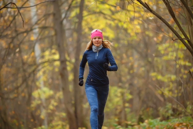 Mujer joven corriendo por la mañana en el bosque de otoño