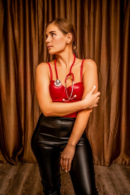 Mujer joven en corsé rojo y pantalones de cuero negro con una enfermera morena sexy fonendoscopio en rojo