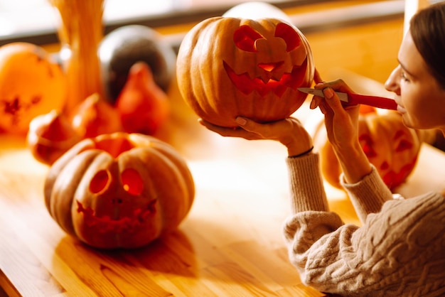 Mujer joven cortando con la cara del personaje del cuchillo en la preparación del objeto de calabaza para la fiesta de halloween