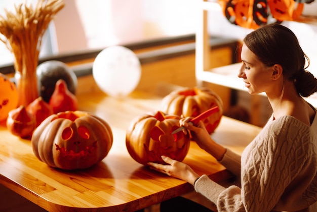 Mujer joven cortando con la cara del personaje del cuchillo en la preparación del objeto de calabaza para la fiesta de halloween