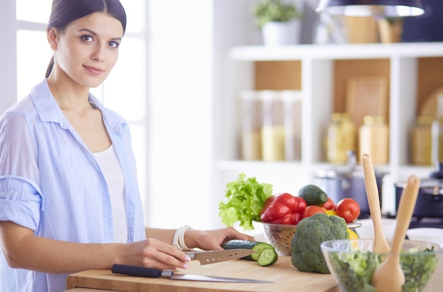 Mujer joven cortando verduras en la cocina de casa