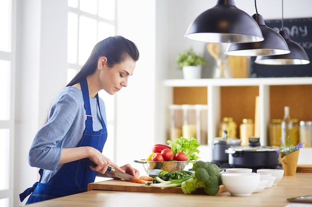 Mujer joven cortando verduras en la cocina de casa