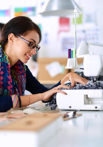 Mujer joven cosiendo mientras está sentada en su lugar de trabajo