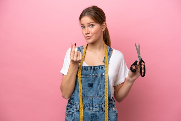 Mujer joven costurera caucásica aislada sobre fondo rosa haciendo gesto de dinero