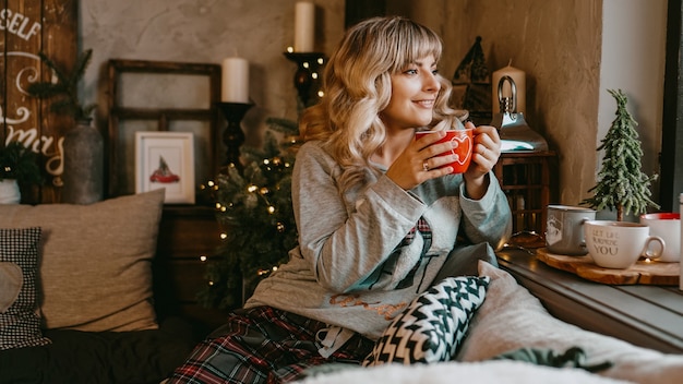 Mujer joven en cuadros con taza de té caliente en un acogedor interior de Navidad. El concepto de preparación para las vacaciones, pide un deseo y sueña.