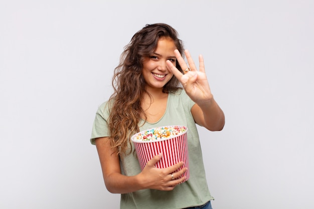 Mujer joven con un cubo pop conrs sonriendo y mirando amigablemente, mostrando el número cuatro o cuarto con la mano hacia adelante, contando hacia atrás