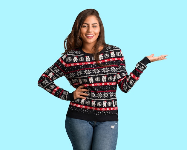 Mujer joven de cuerpo completo con un jersey de Navidad sosteniendo algo con la mano